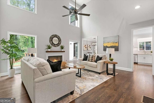 living room featuring dark hardwood / wood-style flooring, a towering ceiling, ceiling fan with notable chandelier, and sink