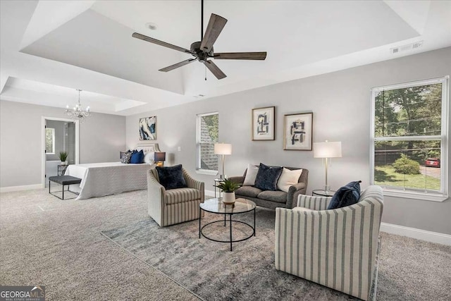 living room featuring carpet flooring, ceiling fan with notable chandelier, and a raised ceiling