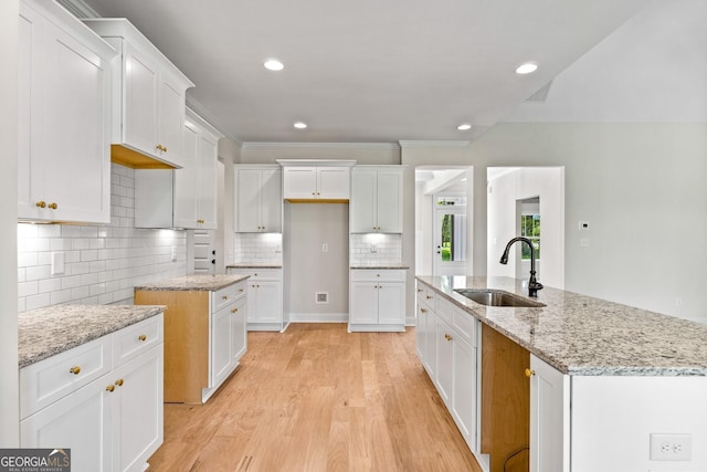 kitchen featuring white cabinets, sink, light hardwood / wood-style floors, and an island with sink