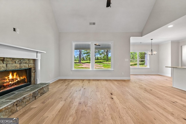 unfurnished living room with a fireplace, ceiling fan with notable chandelier, high vaulted ceiling, and light hardwood / wood-style flooring