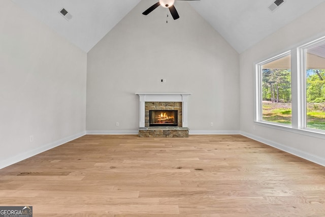 unfurnished living room featuring ceiling fan, light hardwood / wood-style floors, a stone fireplace, and high vaulted ceiling