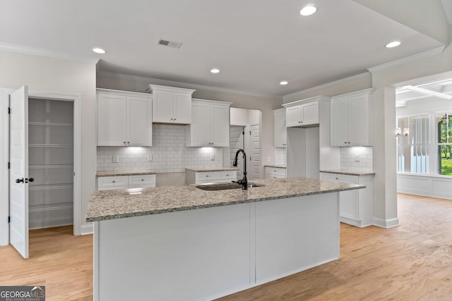 kitchen with light stone countertops, sink, white cabinets, and an island with sink