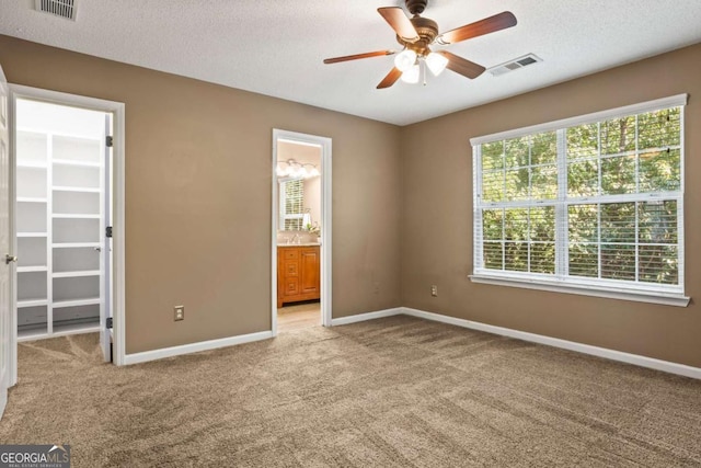 unfurnished bedroom featuring ensuite bath, ceiling fan, a spacious closet, light colored carpet, and a textured ceiling