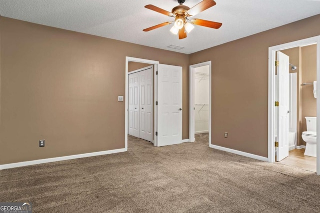 unfurnished bedroom with a walk in closet, ensuite bath, carpet flooring, ceiling fan, and a textured ceiling