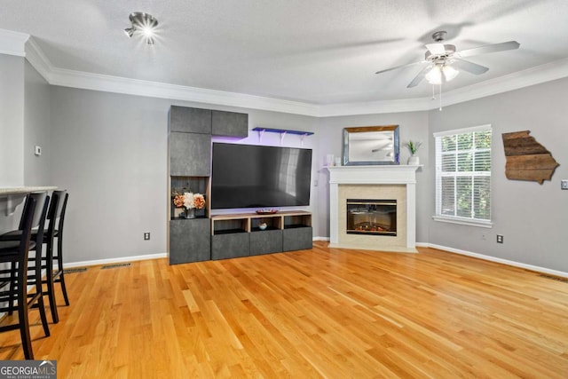 living room featuring crown molding, a textured ceiling, a tile fireplace, and light hardwood / wood-style flooring