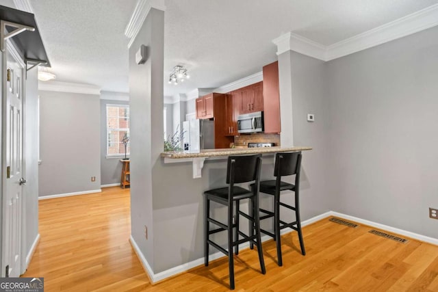 kitchen featuring stainless steel appliances, tasteful backsplash, kitchen peninsula, crown molding, and a kitchen bar