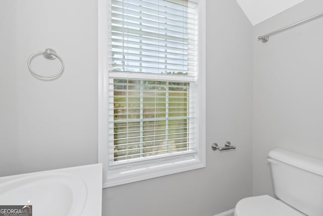 bathroom featuring toilet, plenty of natural light, lofted ceiling, and sink