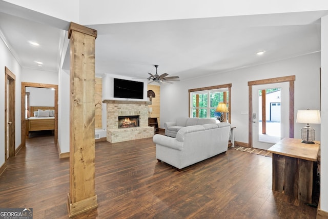 living room with dark hardwood / wood-style floors, ceiling fan, a stone fireplace, and ornamental molding