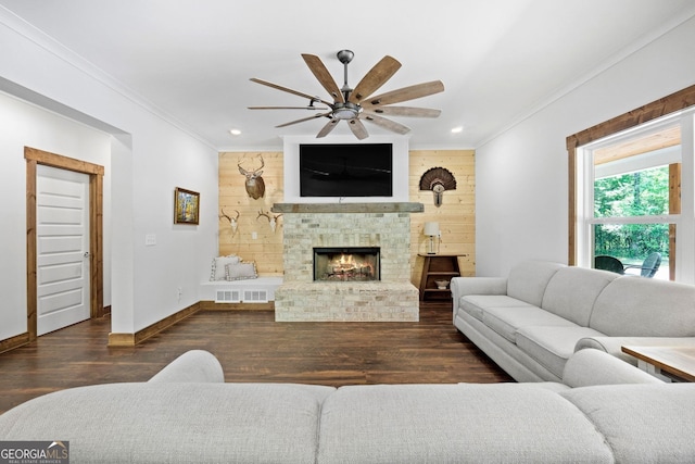 living room with ceiling fan, a stone fireplace, crown molding, and dark wood-type flooring