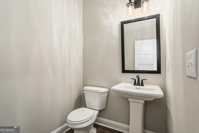 half bath with toilet, baseboards, and wood finished floors