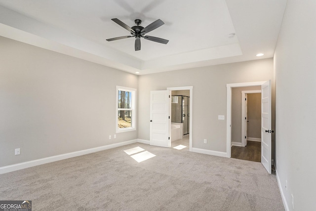 unfurnished bedroom with carpet floors, baseboards, a tray ceiling, and connected bathroom