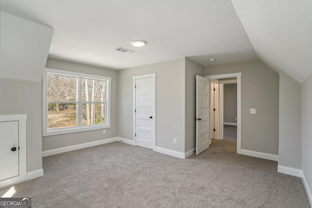 unfurnished bedroom with lofted ceiling, baseboards, visible vents, and light colored carpet