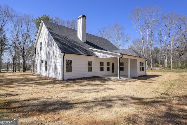 back of property featuring a patio area, a yard, a chimney, and roof with shingles