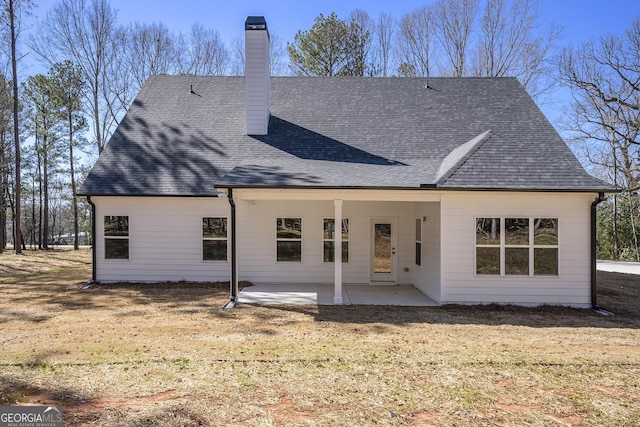 rear view of property with a patio area, a shingled roof, a chimney, and a yard