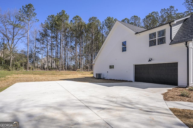 view of side of property with central air condition unit, a garage, and concrete driveway