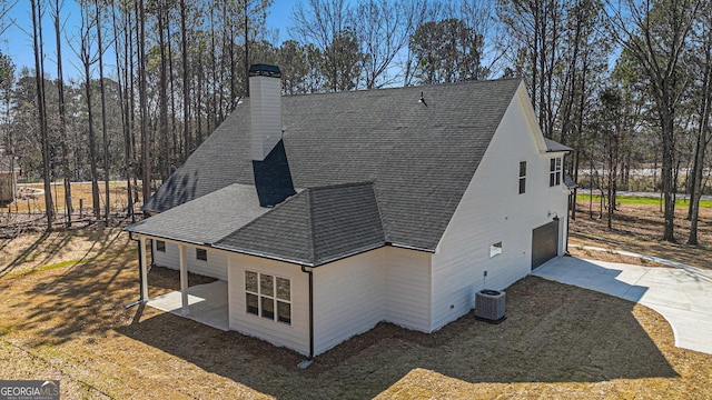 view of side of property featuring central AC unit, a garage, driveway, roof with shingles, and a chimney