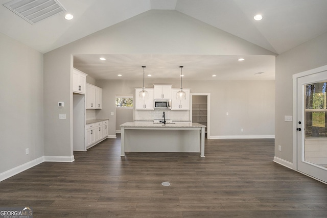 kitchen with a center island with sink, visible vents, stainless steel microwave, hanging light fixtures, and white cabinetry