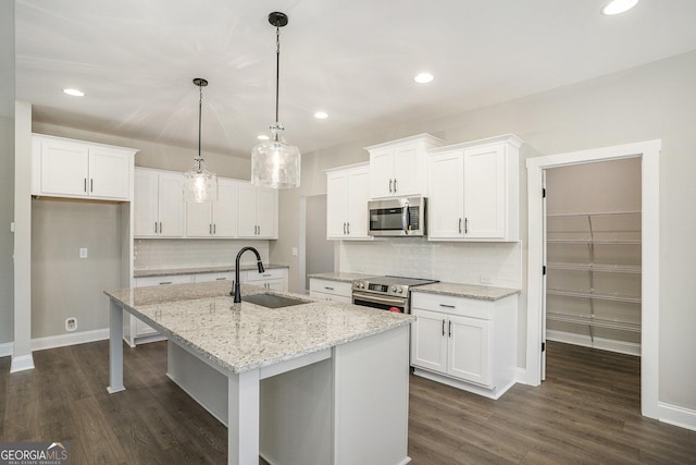 kitchen with stainless steel appliances, hanging light fixtures, white cabinets, a sink, and an island with sink