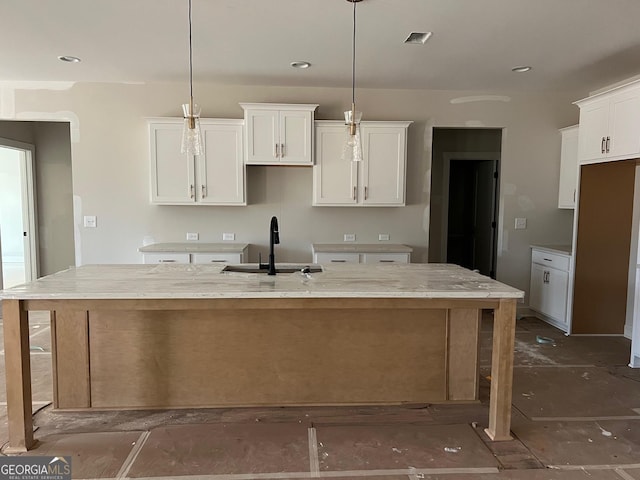 kitchen featuring pendant lighting, sink, white cabinetry, and an island with sink