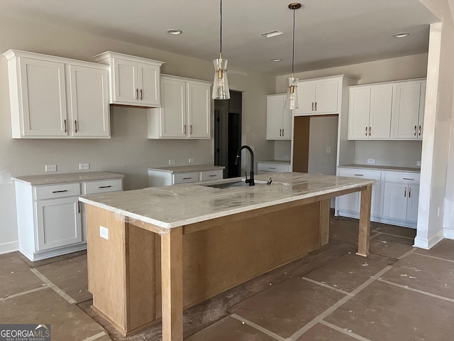 kitchen with white cabinetry, light stone countertops, and an island with sink