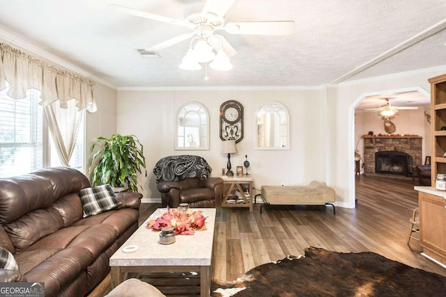 living room featuring a textured ceiling, hardwood / wood-style flooring, a stone fireplace, and crown molding