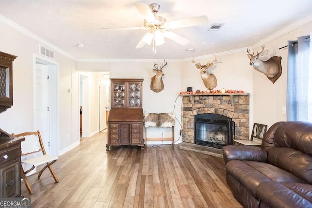 living room featuring hardwood / wood-style floors, a stone fireplace, ceiling fan, and crown molding