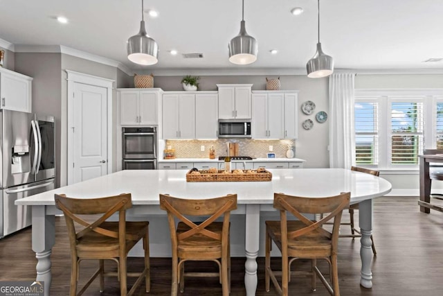 kitchen featuring a large island with sink, hanging light fixtures, appliances with stainless steel finishes, tasteful backsplash, and white cabinetry