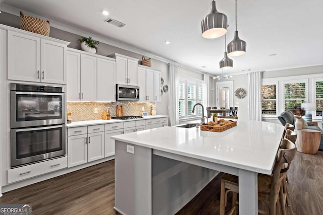 kitchen with decorative light fixtures, sink, an island with sink, and stainless steel appliances