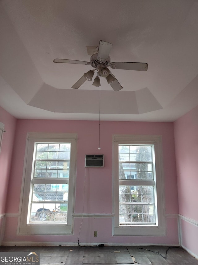 room details with a raised ceiling, a wall mounted AC, and ceiling fan