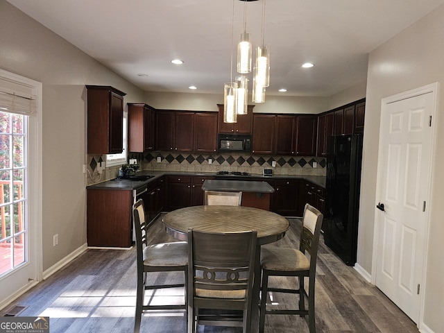 kitchen featuring hanging light fixtures, backsplash, dark brown cabinets, black appliances, and dark hardwood / wood-style flooring