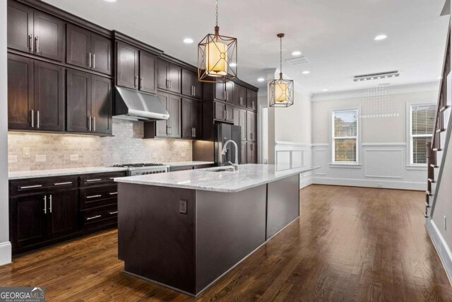 kitchen with light stone counters, dark brown cabinets, decorative light fixtures, dark hardwood / wood-style floors, and an island with sink