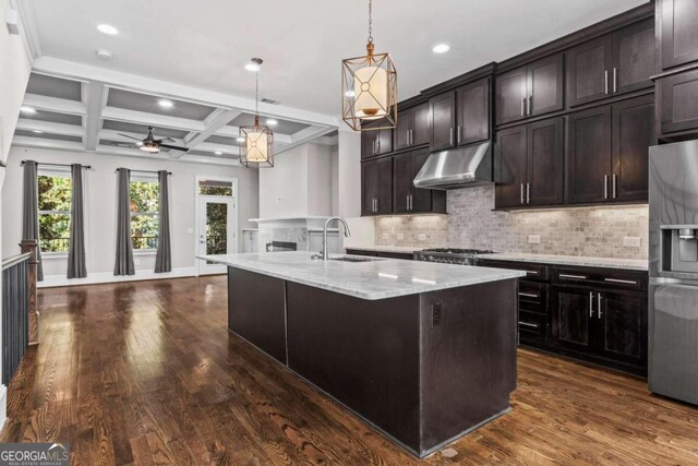 kitchen with sink, coffered ceiling, beamed ceiling, stainless steel fridge, and a kitchen island with sink