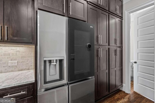 kitchen with stainless steel refrigerator with ice dispenser, dark brown cabinetry, dark wood-type flooring, and backsplash