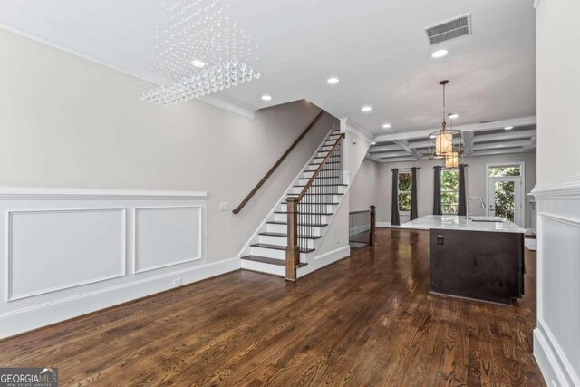 kitchen featuring pendant lighting, dark wood-type flooring, an inviting chandelier, a center island with sink, and sink