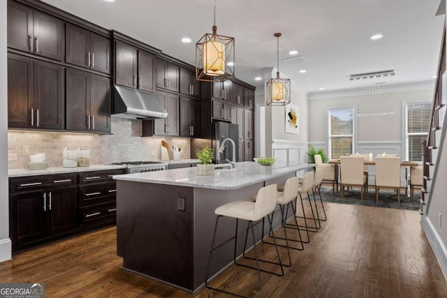 kitchen with a kitchen breakfast bar, crown molding, dark hardwood / wood-style floors, an island with sink, and decorative light fixtures