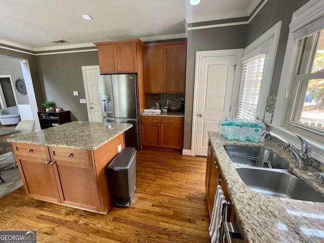 kitchen featuring a center island, sink, light stone countertops, and stainless steel refrigerator with ice dispenser