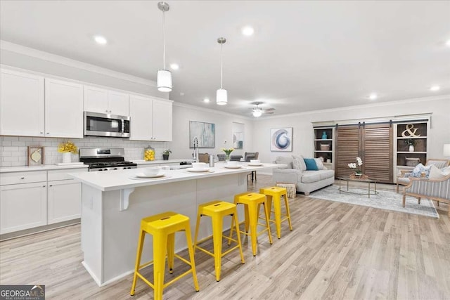 kitchen featuring pendant lighting, stainless steel appliances, white cabinetry, and a kitchen island with sink