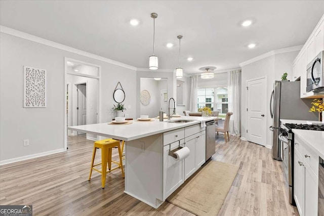 kitchen featuring appliances with stainless steel finishes, a kitchen island with sink, sink, decorative light fixtures, and white cabinetry