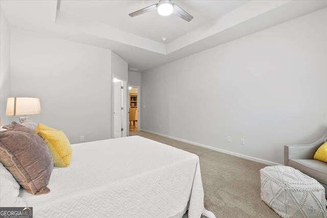 carpeted bedroom with a raised ceiling and ceiling fan