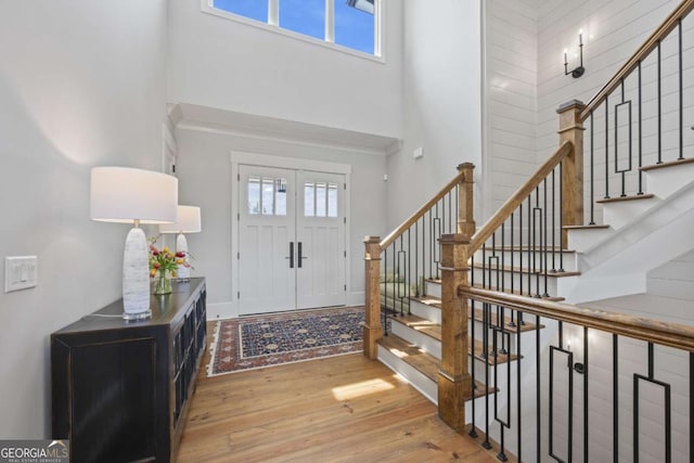 foyer featuring french doors, a towering ceiling, light hardwood / wood-style flooring, and a healthy amount of sunlight