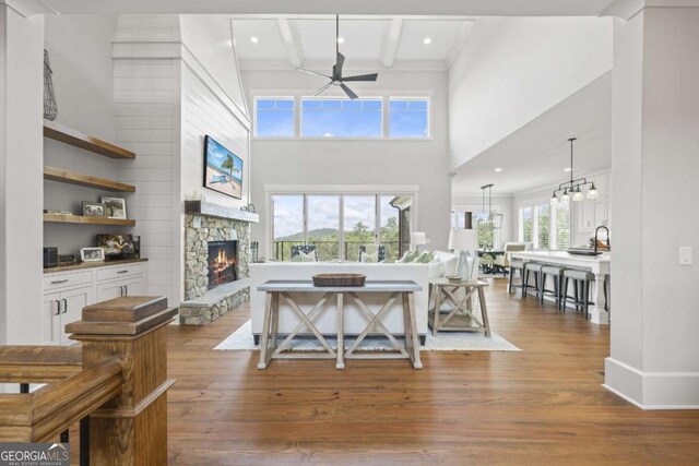 living room with ceiling fan, beam ceiling, a fireplace, and light hardwood / wood-style flooring