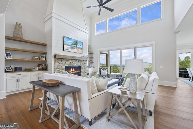 living room with a stone fireplace, ceiling fan, plenty of natural light, and hardwood / wood-style flooring