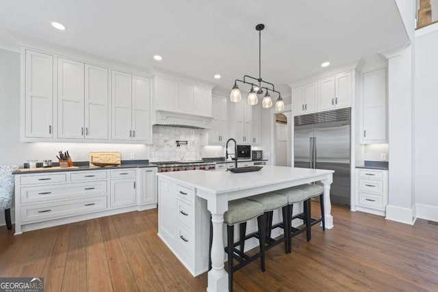 kitchen with white cabinetry, hanging light fixtures, a kitchen breakfast bar, a kitchen island with sink, and appliances with stainless steel finishes