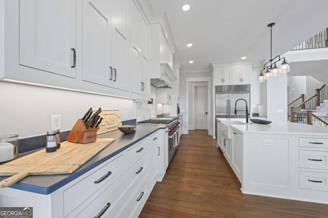 kitchen featuring high end appliances, decorative light fixtures, white cabinets, dark hardwood / wood-style floors, and an island with sink