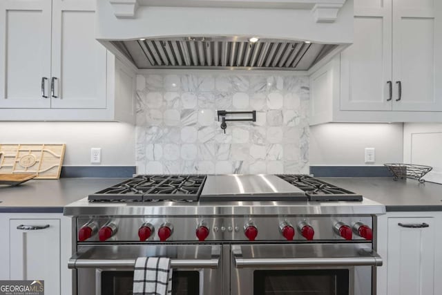 kitchen featuring decorative backsplash, white cabinets, range with two ovens, and wall chimney range hood