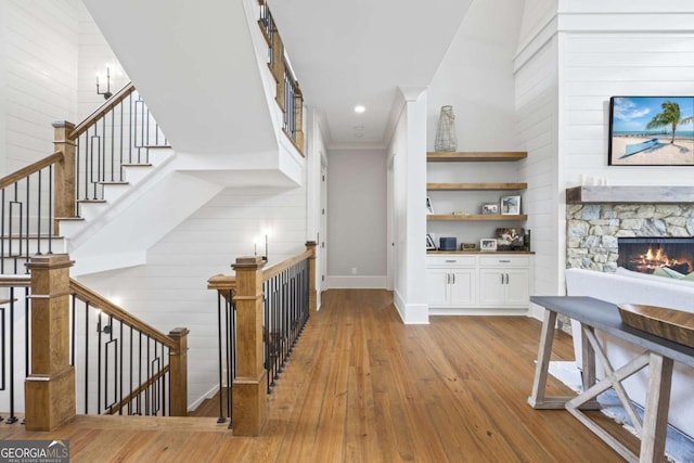 bar featuring a towering ceiling, crown molding, light hardwood / wood-style flooring, white cabinetry, and a stone fireplace