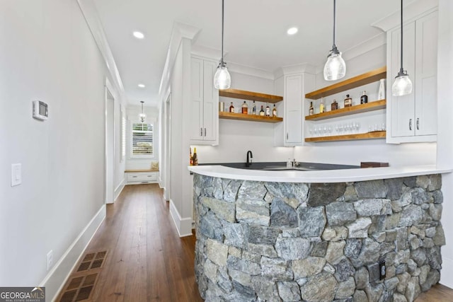 bar featuring dark hardwood / wood-style flooring, decorative light fixtures, white cabinetry, and ornamental molding