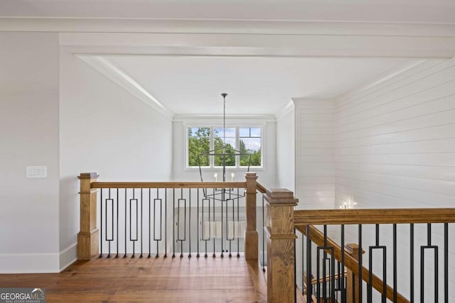 hallway with hardwood / wood-style flooring, ornamental molding, and an inviting chandelier