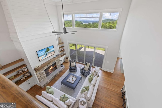 living room with hardwood / wood-style floors, a stone fireplace, ceiling fan, and a healthy amount of sunlight