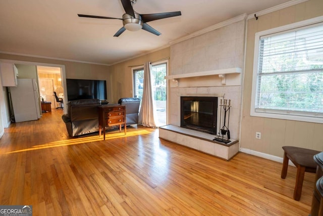 living room featuring ceiling fan, crown molding, hardwood / wood-style floors, plenty of natural light, and a tiled fireplace